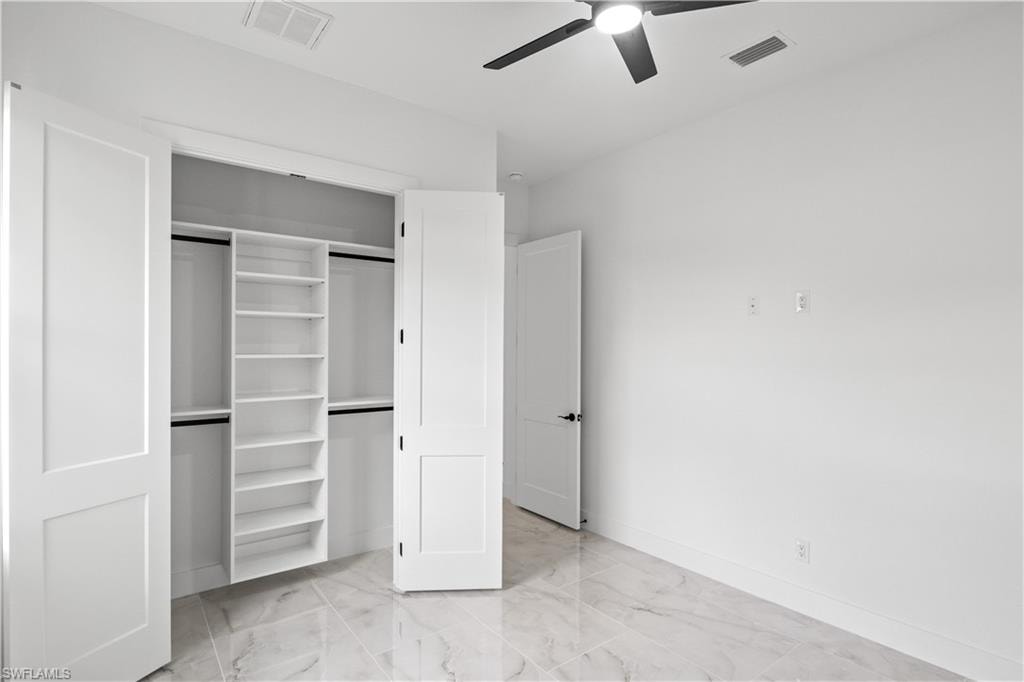 Unfurnished bedroom featuring light marble finish floors, a closet, and a ceiling fan