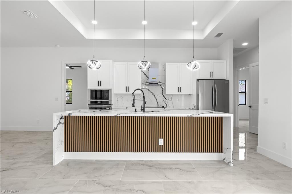 Kitchen with a spacious island, light stone counters, white cabinetry, hanging light fixtures, and a tray ceiling