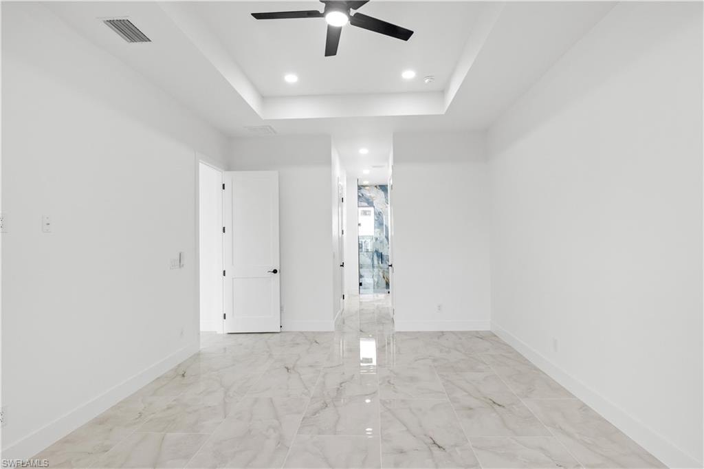 Unfurnished room featuring a raised ceiling, a ceiling fan, light marble finish flooring, and recessed lighting