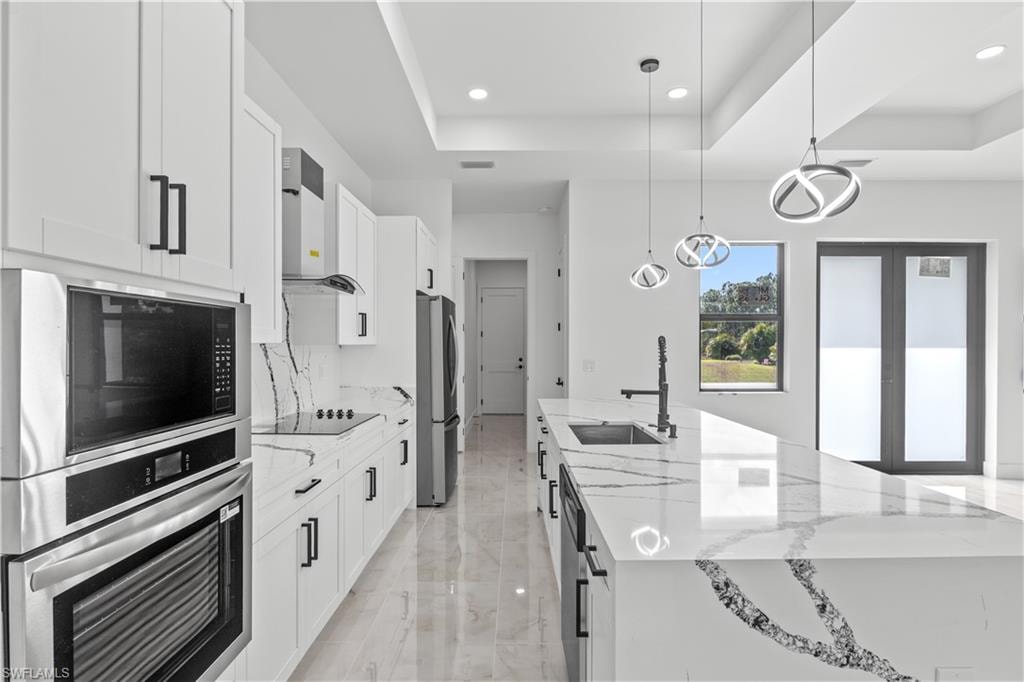 Kitchen featuring appliances with stainless steel finishes, light stone counters, decorative light fixtures, white cabinets, and recessed lighting