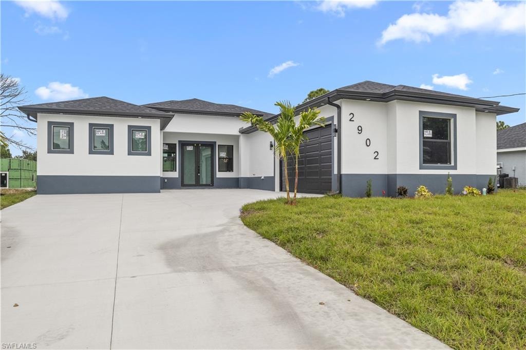 Prairie-style home with stucco siding, a front yard, an attached garage, and concrete driveway