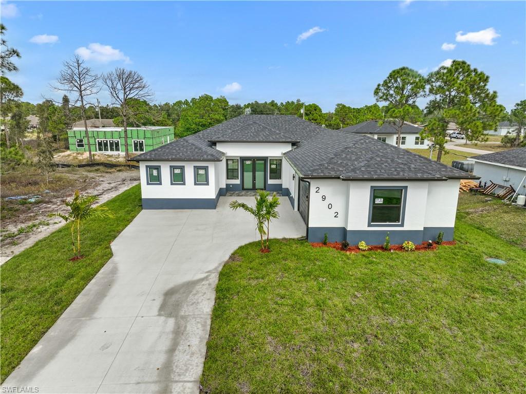 Prairie-style home with a shingled roof, stucco siding, concrete driveway, and a front yard