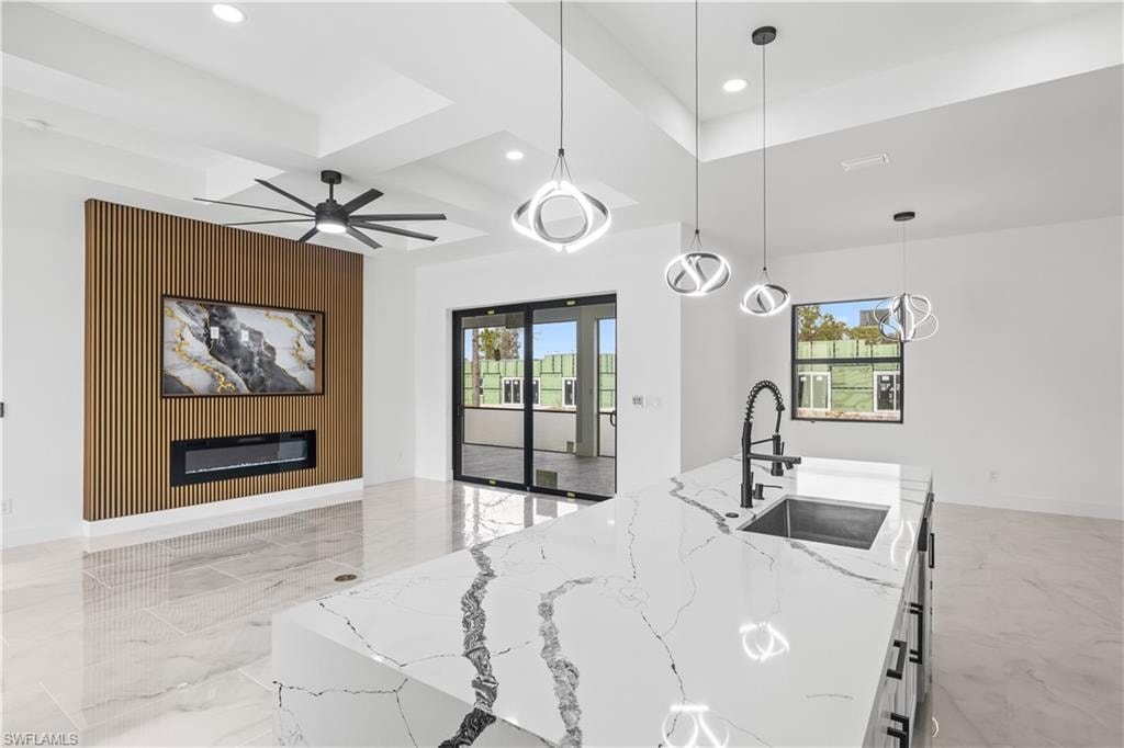 Kitchen featuring decorative light fixtures, healthy amount of natural light, light marble finish floors, light stone countertops, and coffered ceiling