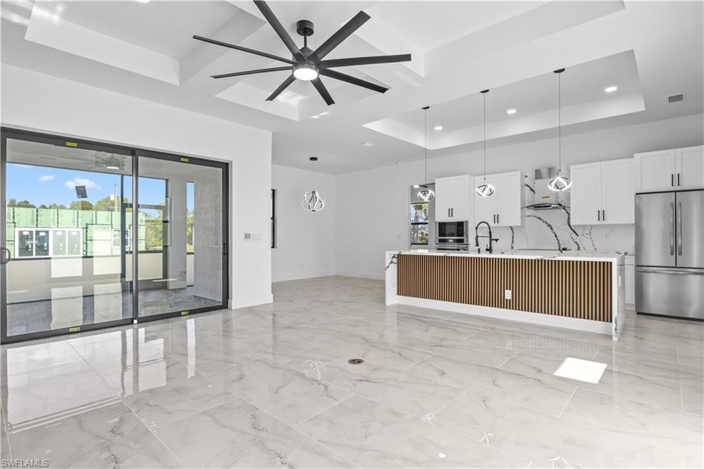 Kitchen with freestanding refrigerator, hanging light fixtures, white cabinets, light stone countertops, and a center island with sink