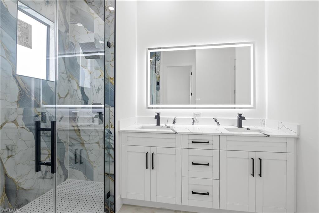 Full bath with double vanity and a marble finish shower