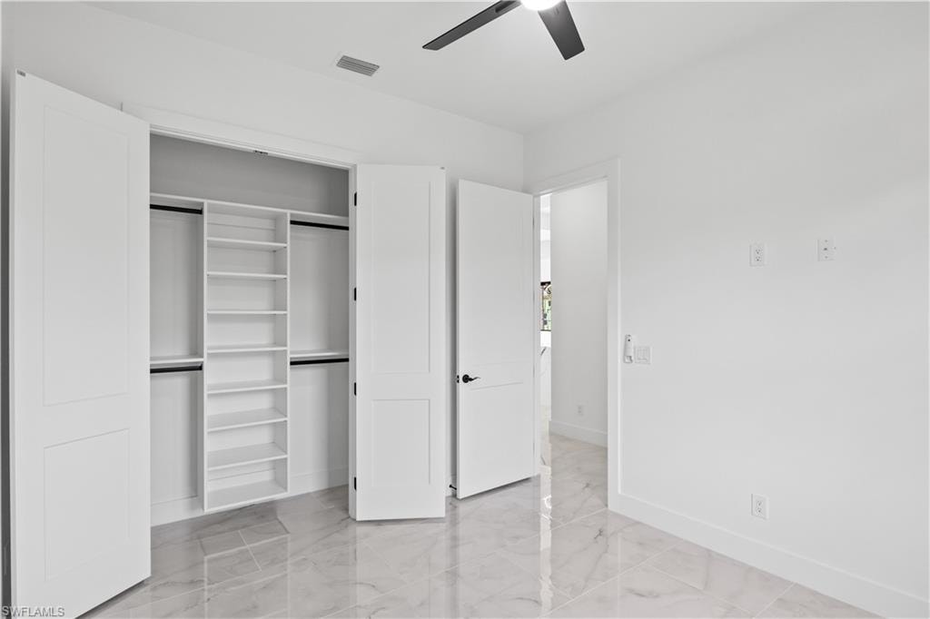 Unfurnished bedroom with light marble finish flooring, a closet, and ceiling fan
