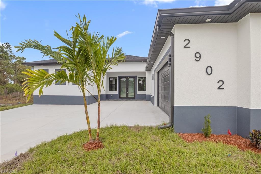 Entrance to property featuring french doors, stucco siding, a lawn, and driveway