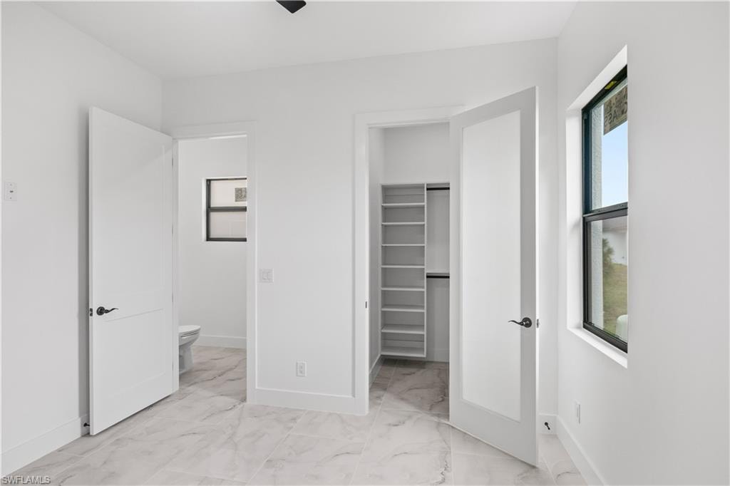 Unfurnished bedroom featuring a spacious closet, light marble finish flooring, and ceiling fan