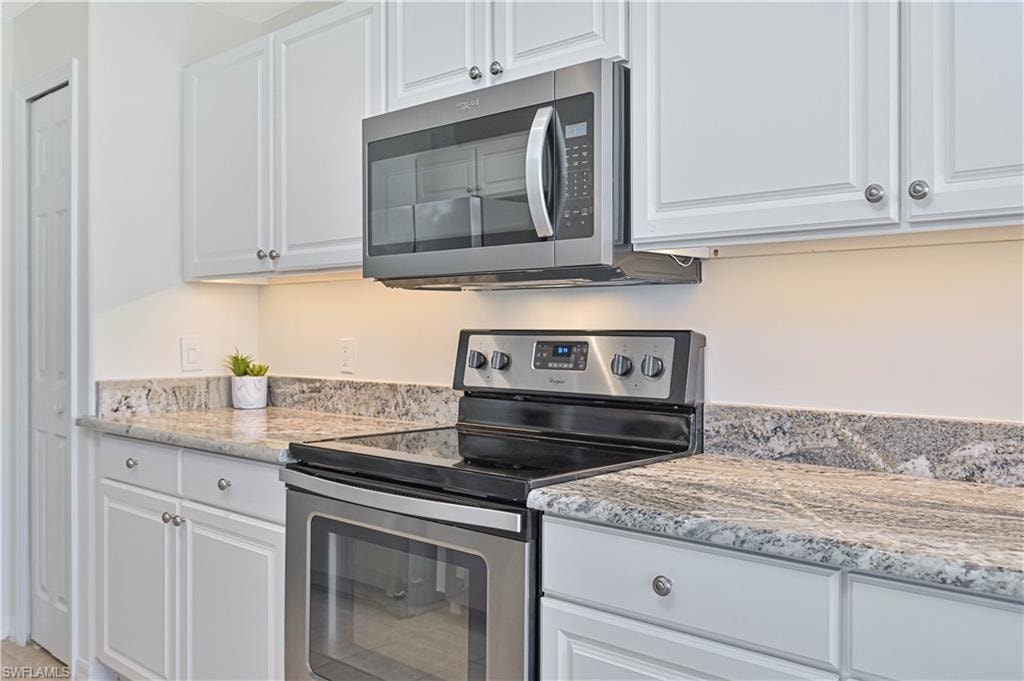 Kitchen with stainless steel appliances, white cabinetry, and light stone countertops