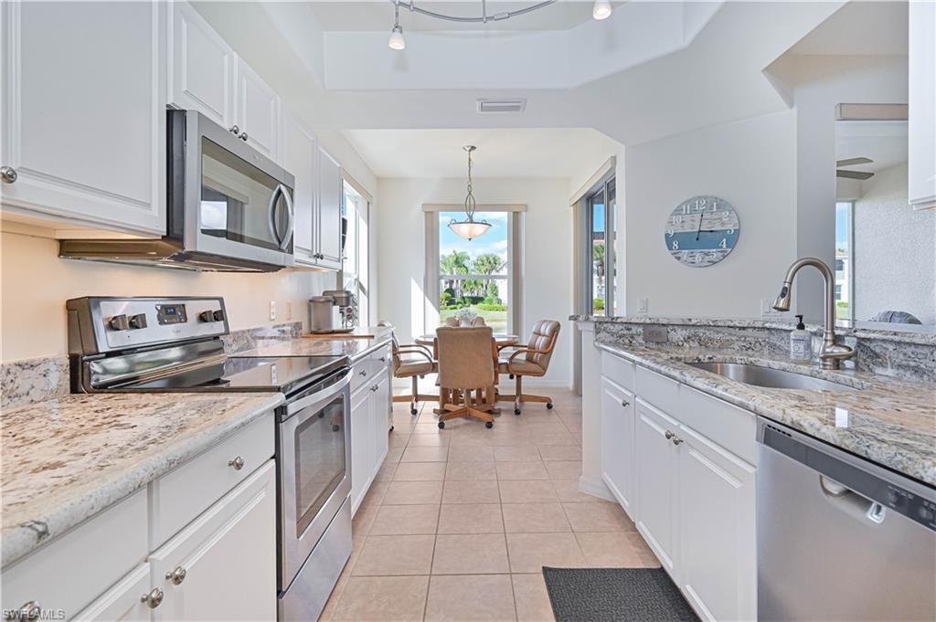 Kitchen featuring appliances with stainless steel finishes, light stone counters, white cabinets, and light tile patterned floors