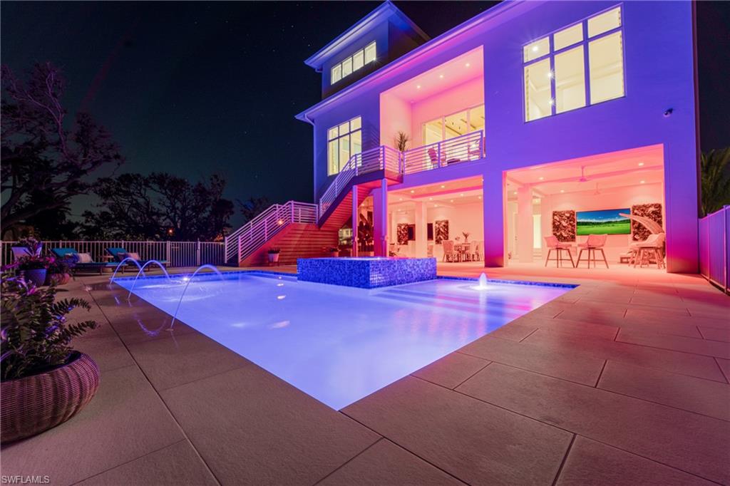 Pool at night with stairs, a balcony, an outdoor pool, a patio area, and a jacuzzi