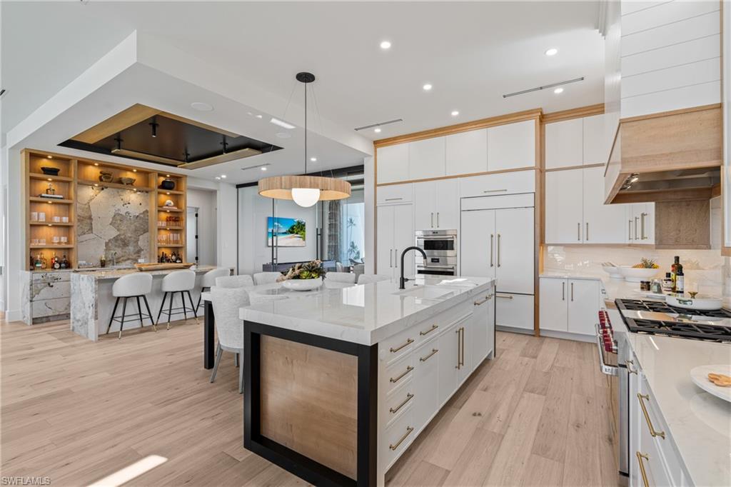 Kitchen with light stone counters, high quality appliances, a large island with sink, hanging light fixtures, and recessed lighting