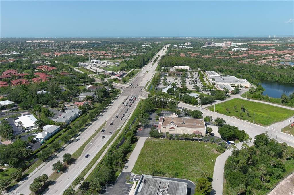 Aerial perspective showcasing a developed corridor with mixed-use properties, a prominent commercial center with ample parking, and an expansive body of water