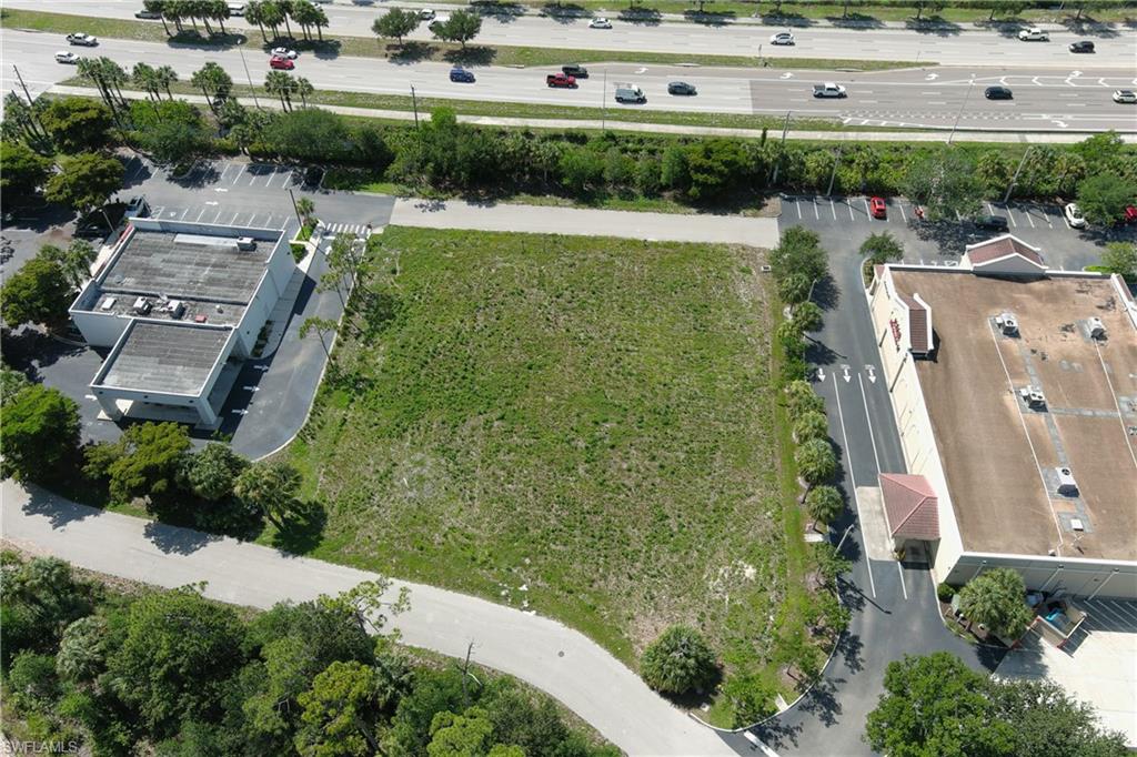 Expansive undeveloped parcel featuring a grass field, bordered by paved parking areas and mature landscaping