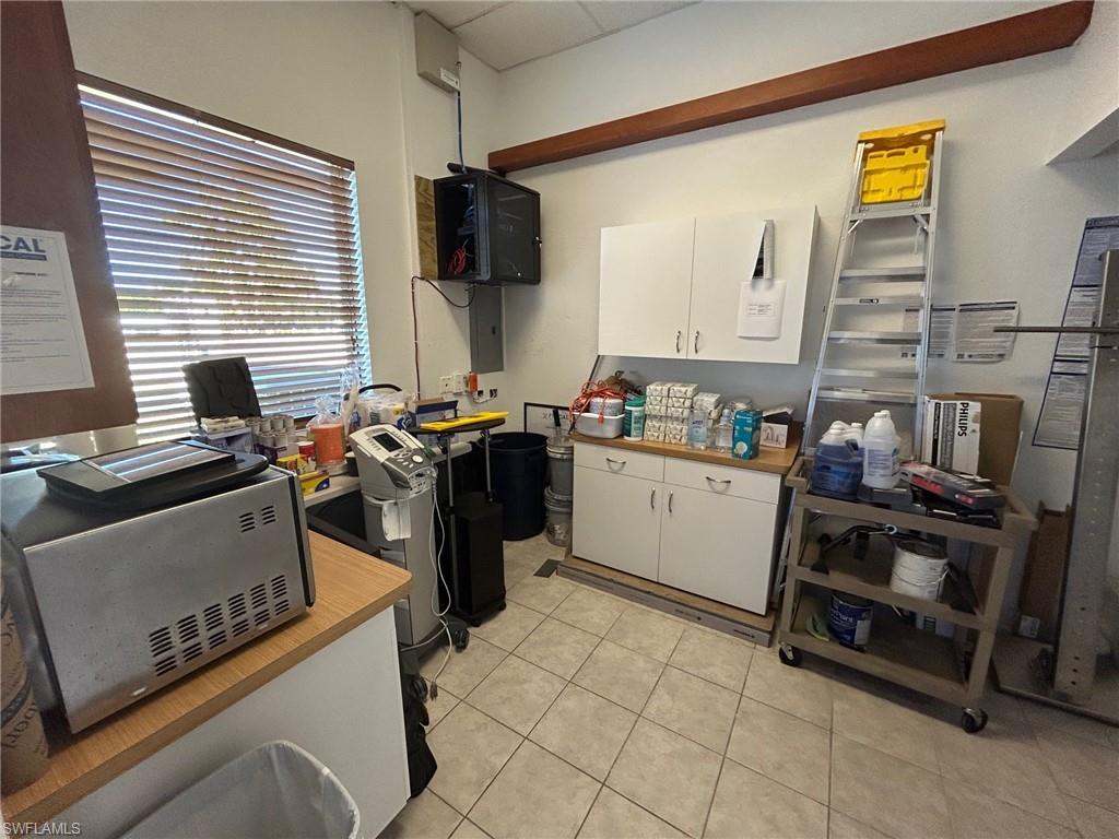 Kitchen with white cabinets, stainless steel microwave, light tile patterned floors, electric panel, and a drop ceiling