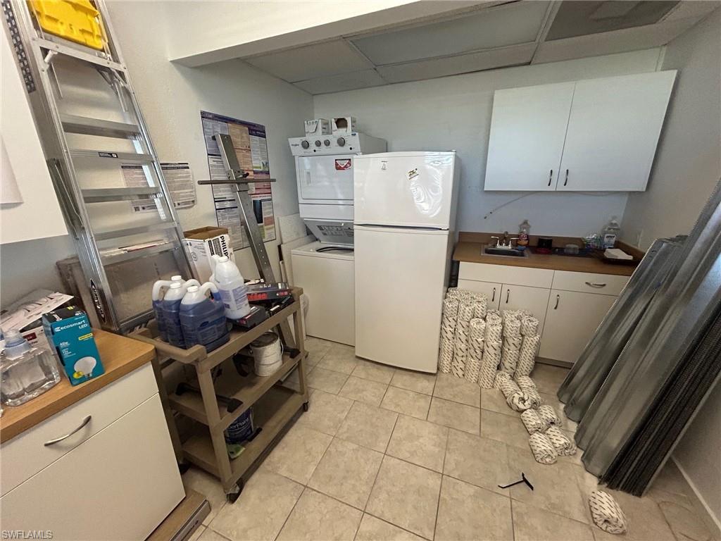 Kitchen with white cabinets, freestanding refrigerator, stacked washer / drying machine, and light tile patterned flooring