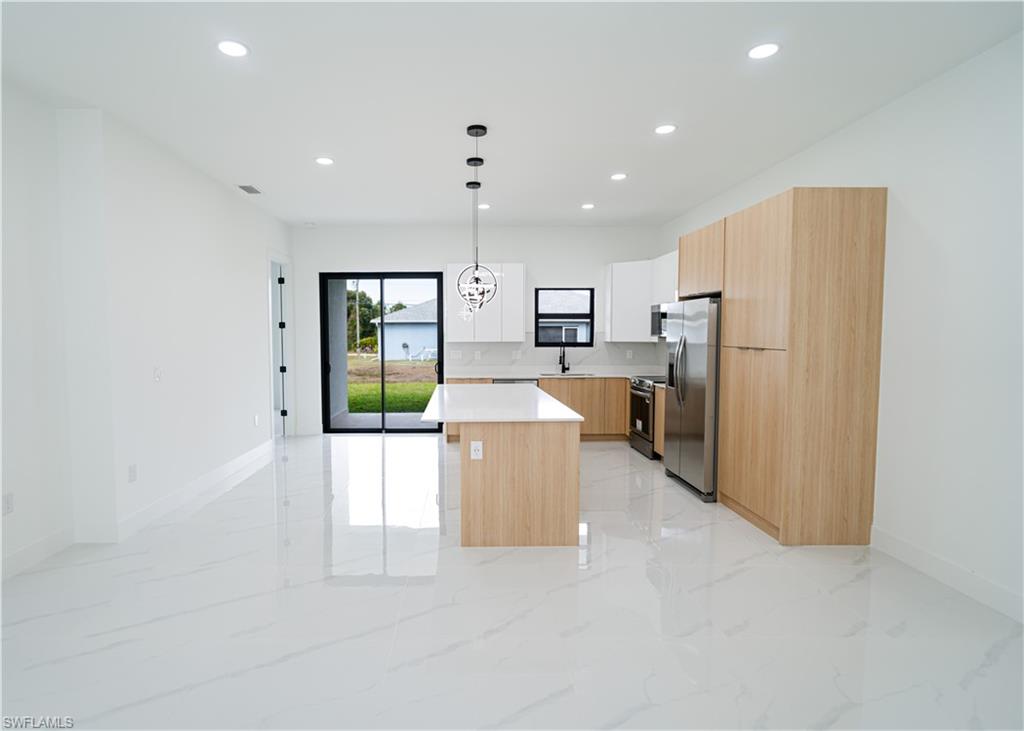 Kitchen featuring modern cabinets, a center island, decorative light fixtures, light brown cabinetry, and appliances with stainless steel finishes