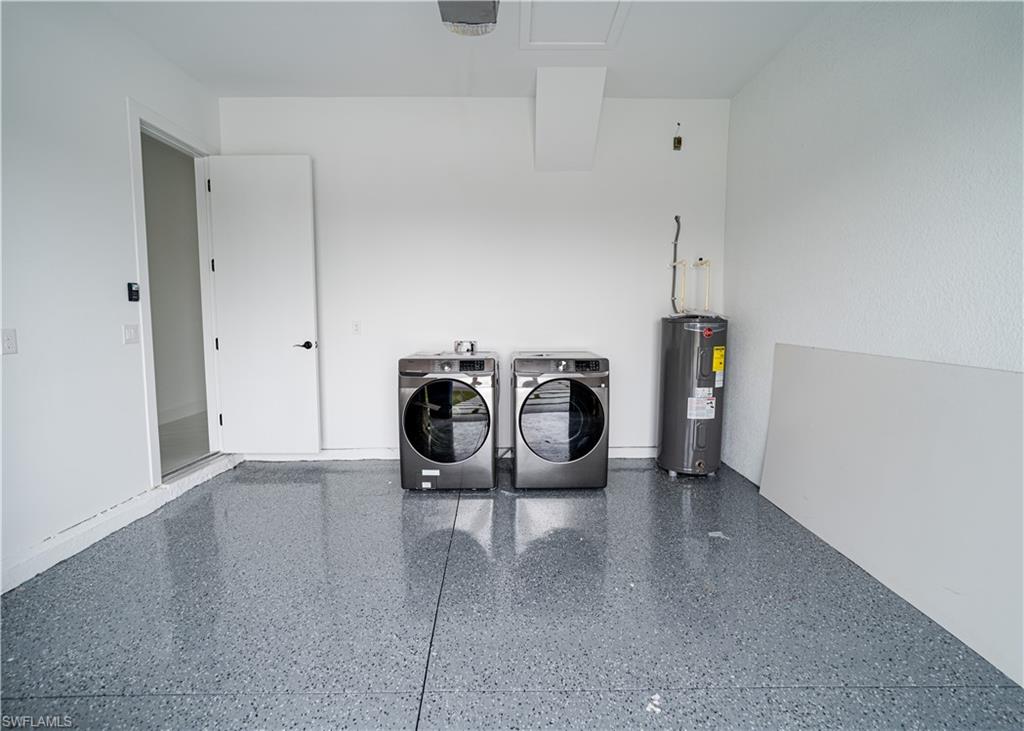 Washroom with washer and clothes dryer, water heater, and a garage