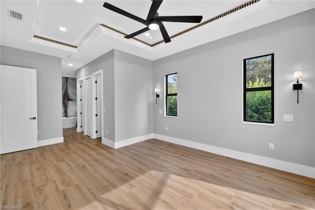 Primary bedroom featuring a tray ceiling, light wood-style flooring, ceiling fan, recessed lighting, and connected bathroom