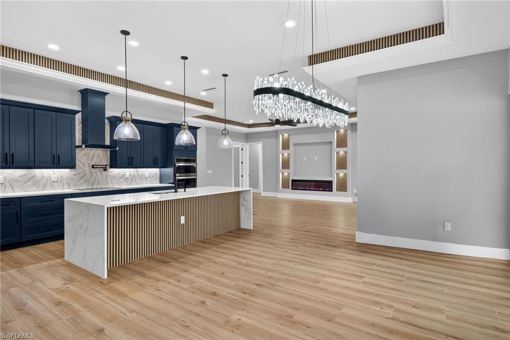 Kitchen with double oven, decorative light fixtures, backsplash, a center island with sink, and light wood-style flooring
