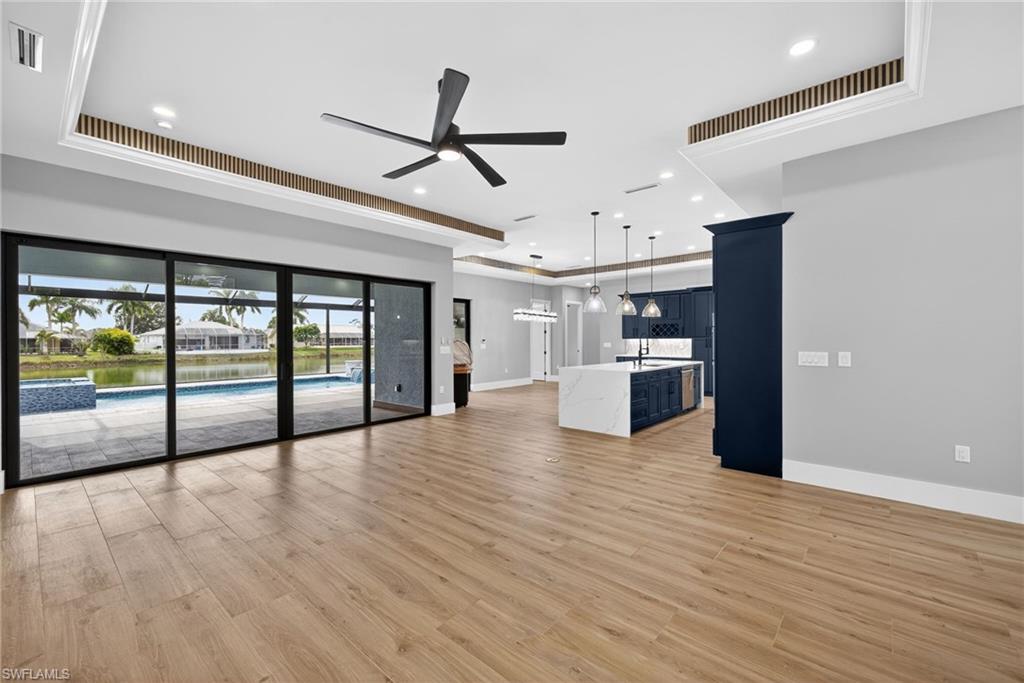 Unfurnished living room with light wood finished floors, a ceiling fan, recessed lighting, and a tray ceiling