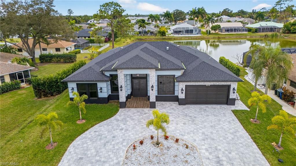 View of front of house featuring a garage, a residential view, decorative driveway, a shingled roof, and a water view