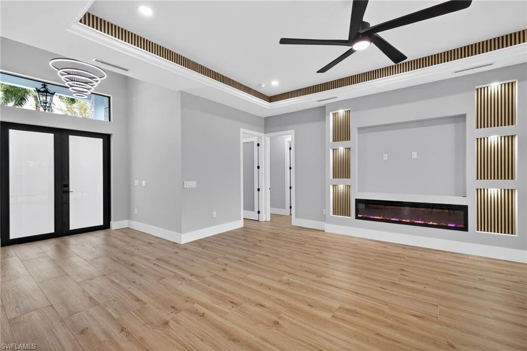 Unfurnished living room with light wood-style floors, french doors, a glass covered fireplace, a raised ceiling, and a ceiling fan