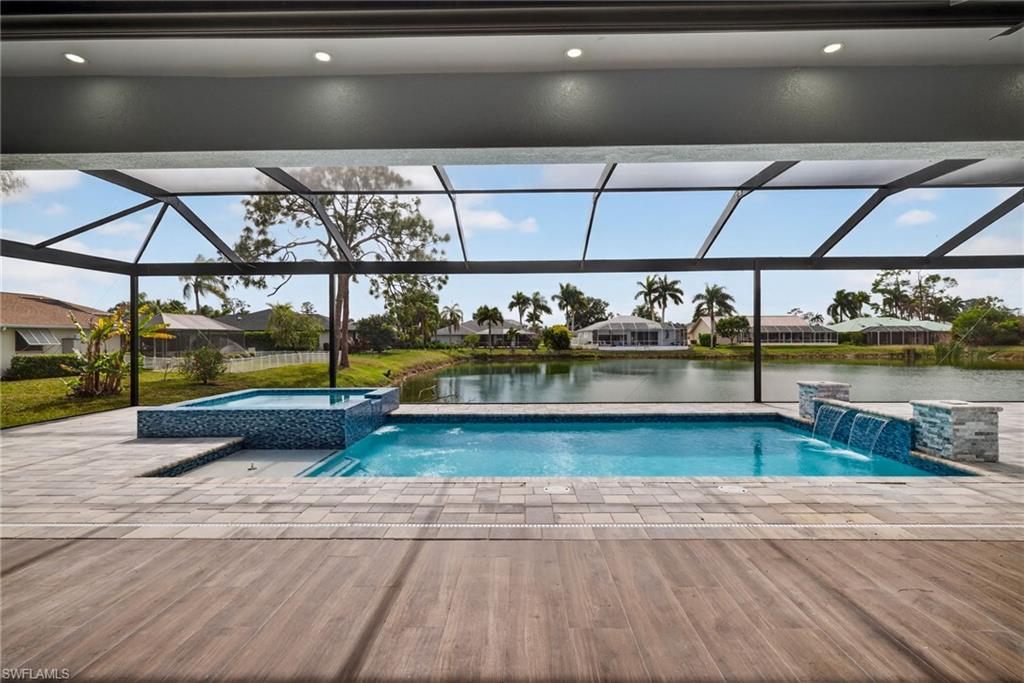View of swimming pool featuring a water view, glass enclosure, a pool with connected hot tub, and a patio area