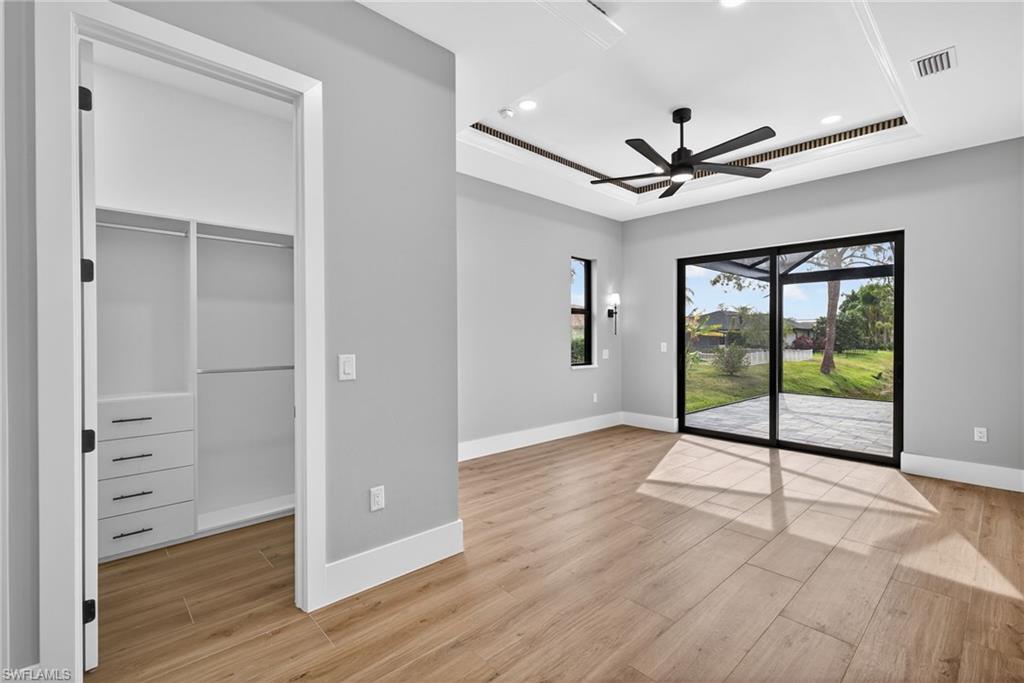 Primary bedroom featuring a raised ceiling, access to exterior, a walk in closet, light wood finished floors, and recessed lighting