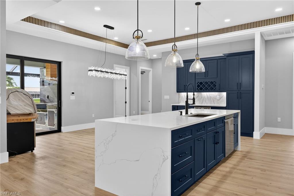 Kitchen with blue cabinetry, a center island with sink, light stone counters, light wood-style floors, and pendant lighting
