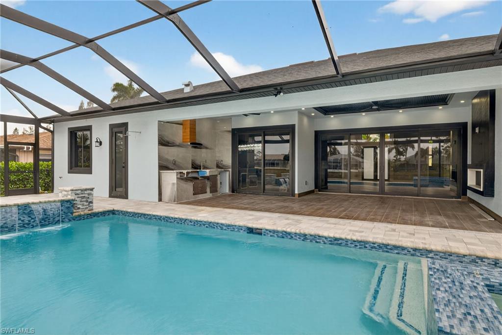 Swimming pool featuring exterior kitchen, a sunroom, glass enclosure, and a patio