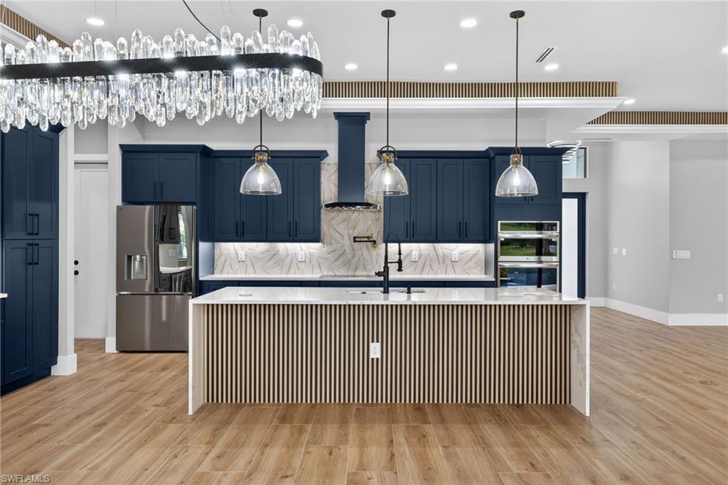 Kitchen with blue cabinetry, a spacious island, backsplash, appliances with stainless steel finishes, and light stone countertops