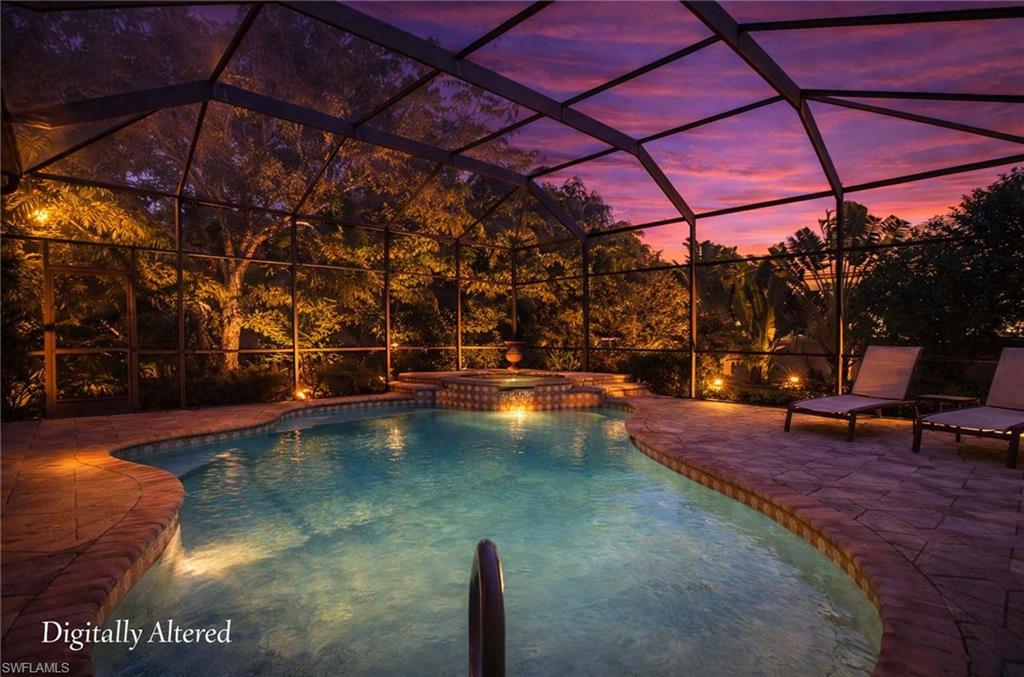 Pool at dusk featuring glass enclosure, a pool with connected hot tub, and a patio area