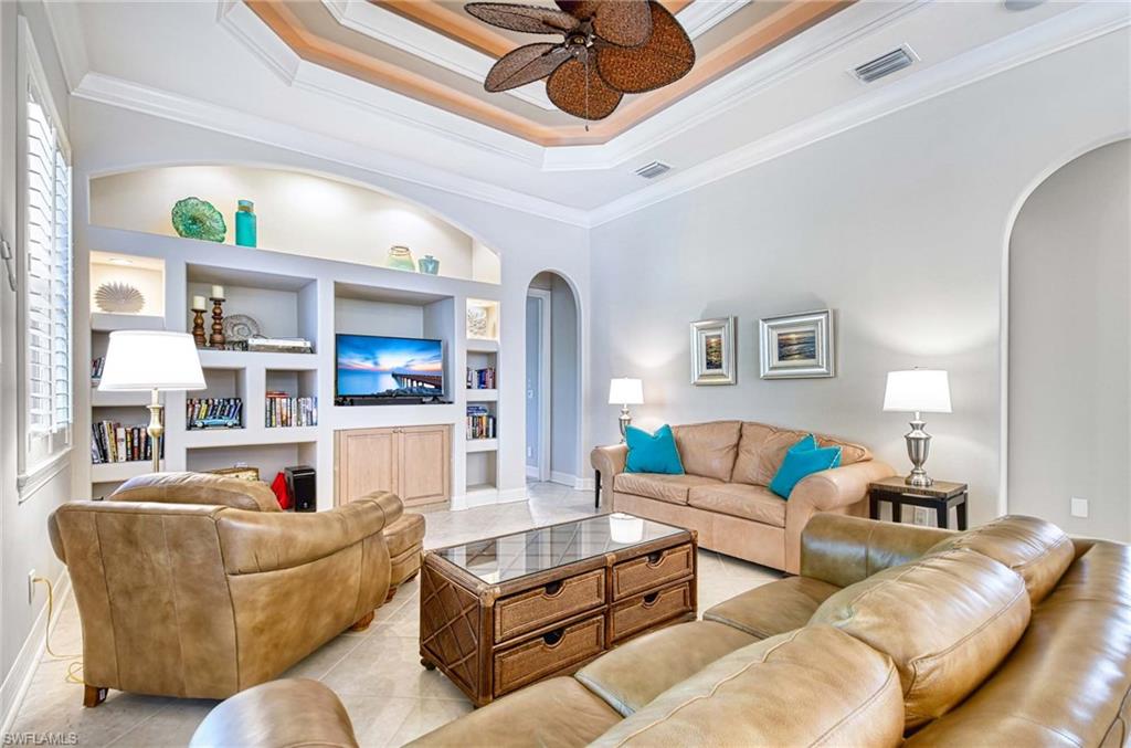 Living room featuring built in features, arched walkways, crown molding, a ceiling fan, and light tile patterned floors