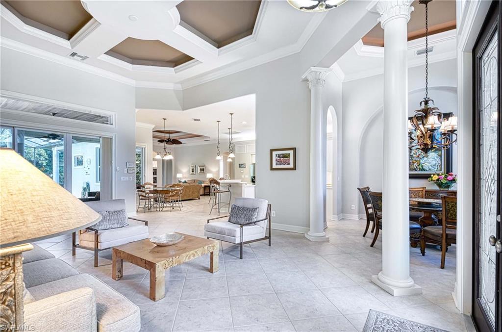 Living room featuring a chandelier, crown molding, decorative columns, a high ceiling, and coffered ceiling