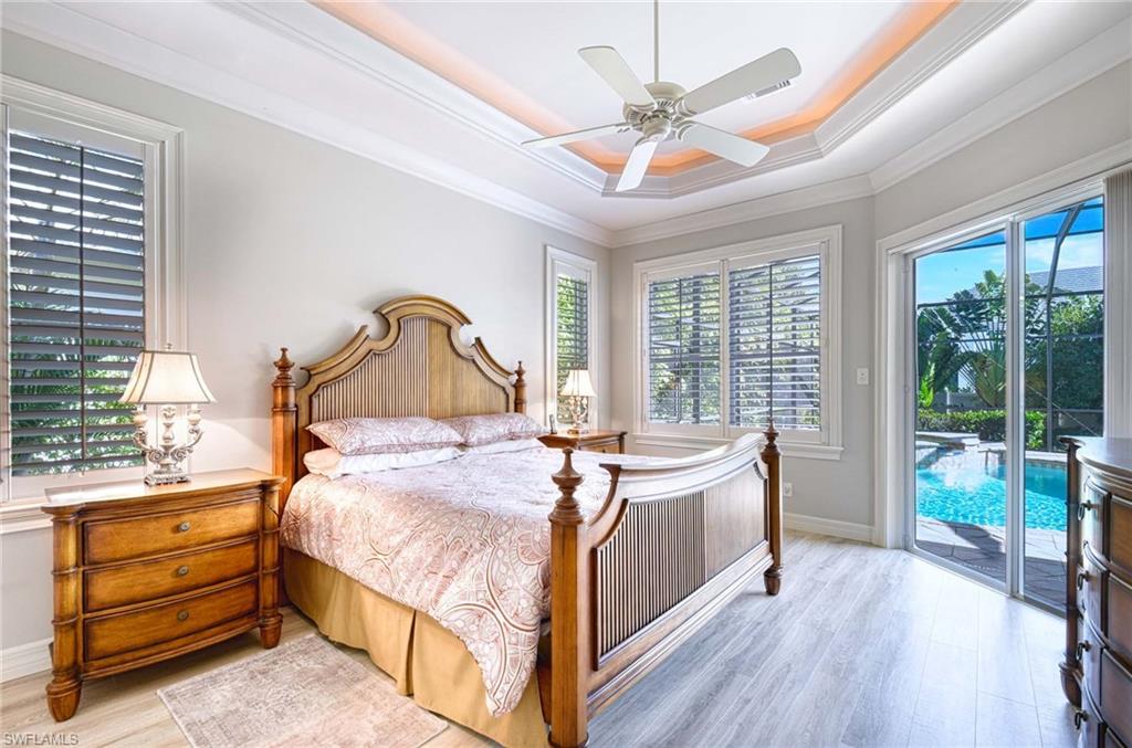 Bedroom featuring wood finished floors, a tray ceiling, access to exterior, ceiling fan, and crown molding