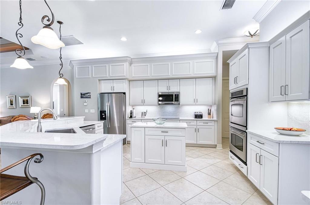 Kitchen featuring crown molding, arched walkways, hanging light fixtures, white cabinets, and appliances with stainless steel finishes