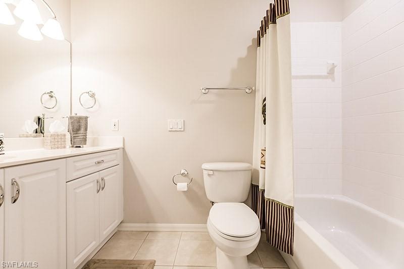 Full bathroom with tile patterned flooring, shower / bath combo with shower curtain, toilet, and vanity