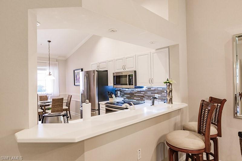 Kitchen featuring white cabinetry, lofted ceiling, a breakfast bar area, stainless steel appliances, and decorative light fixtures