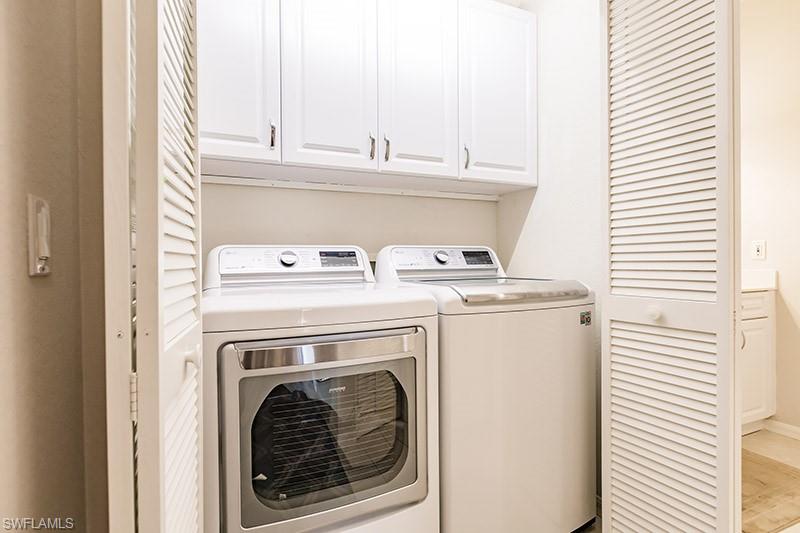 Washroom featuring washing machine and dryer, light hardwood / wood-style flooring, and cabinets