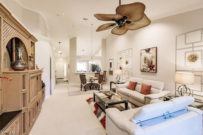 Carpeted living room with crown molding, ceiling fan, and a towering ceiling