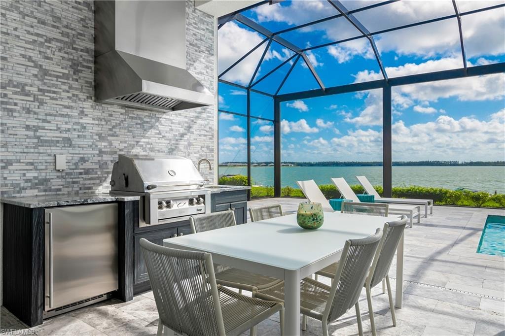 View of patio featuring an outdoor kitchen, outdoor dining area, a sunroom, a lanai, and a water view