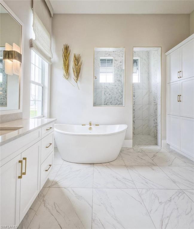 Bathroom with a freestanding bath, vanity, a marble finish shower, and light marble finish flooring