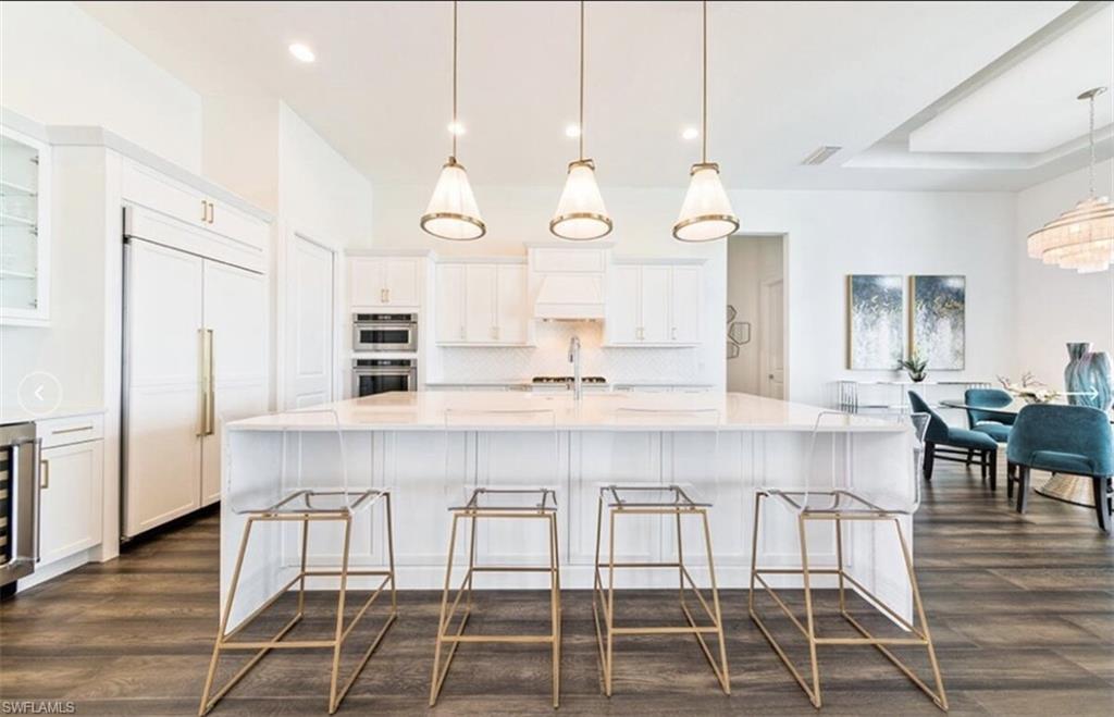 Kitchen with a spacious island, white cabinetry, light stone counters, paneled built in refrigerator, and a breakfast bar area
