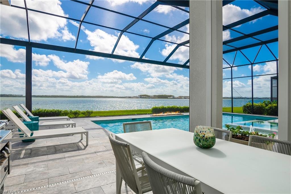 Outdoor pool featuring glass enclosure, a water view, a patio area, outdoor dining space, and a sunroom
