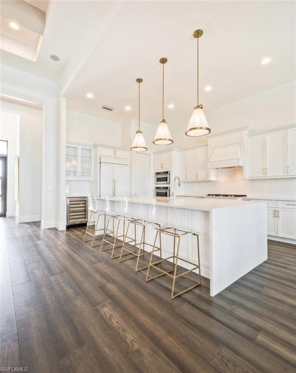 Kitchen with tasteful backsplash, a large island, a breakfast bar area, white cabinets, and decorative light fixtures