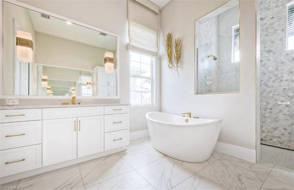 Full bath with a walk in shower, vanity, a freestanding bath, and light marble finish flooring