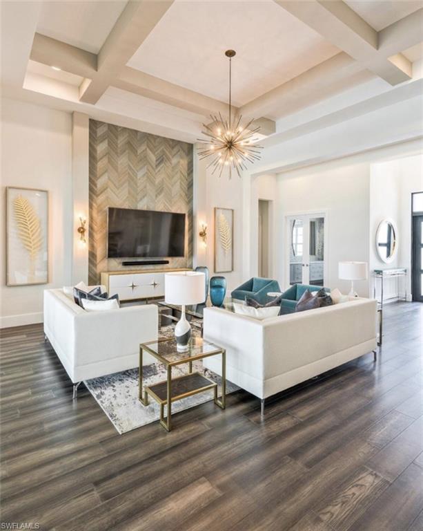 Living area featuring coffered ceiling, beam ceiling, dark wood-style floors, an accent wall, and a chandelier