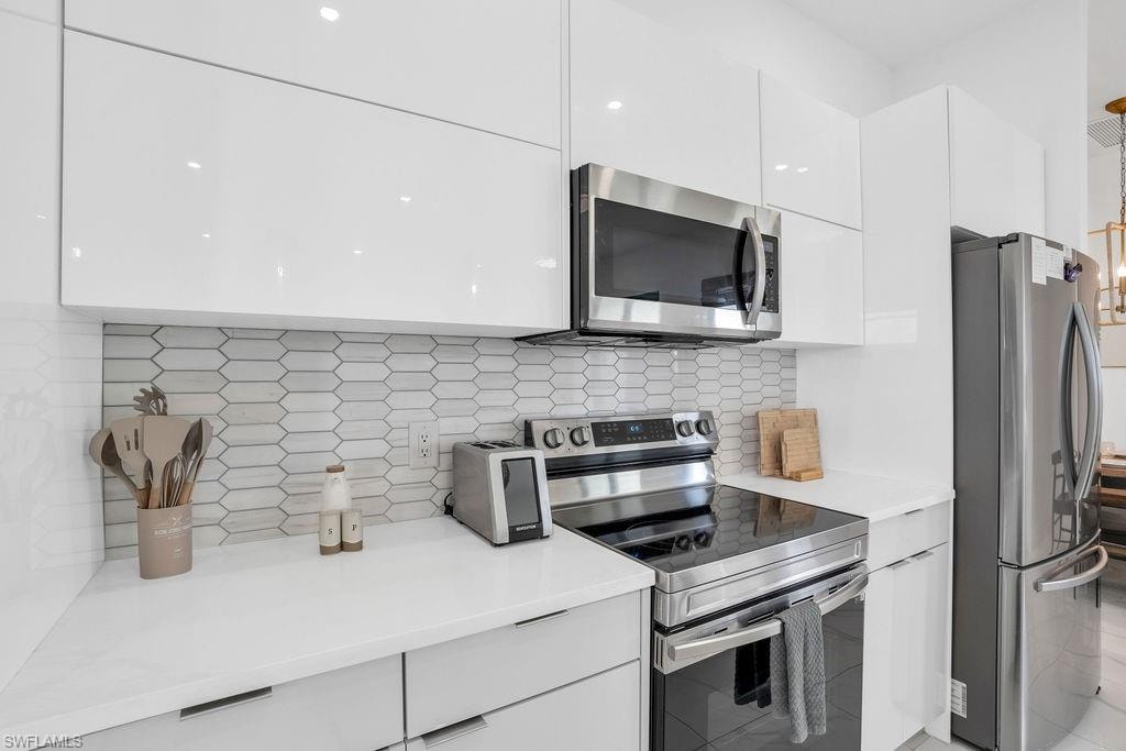 Kitchen with modern cabinets, stainless steel appliances, white cabinetry, decorative backsplash, and light quartz counters