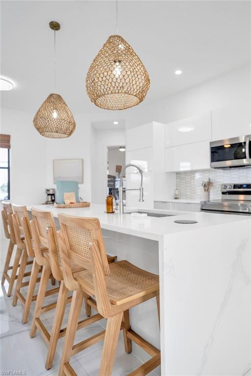 Kitchen with modern cabinets, a kitchen breakfast bar, hanging light fixtures, tasteful backsplash, and appliances with stainless steel finishes